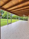 Screened-in patio featuring decorative tile flooring, exposed wood-beam ceiling, ceiling fan, and lawn access