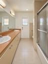Extended vanity with dual undermount sinks, solid-surface countertop, full-width wall mirror, and tub-shower combination with sliding textured glass d