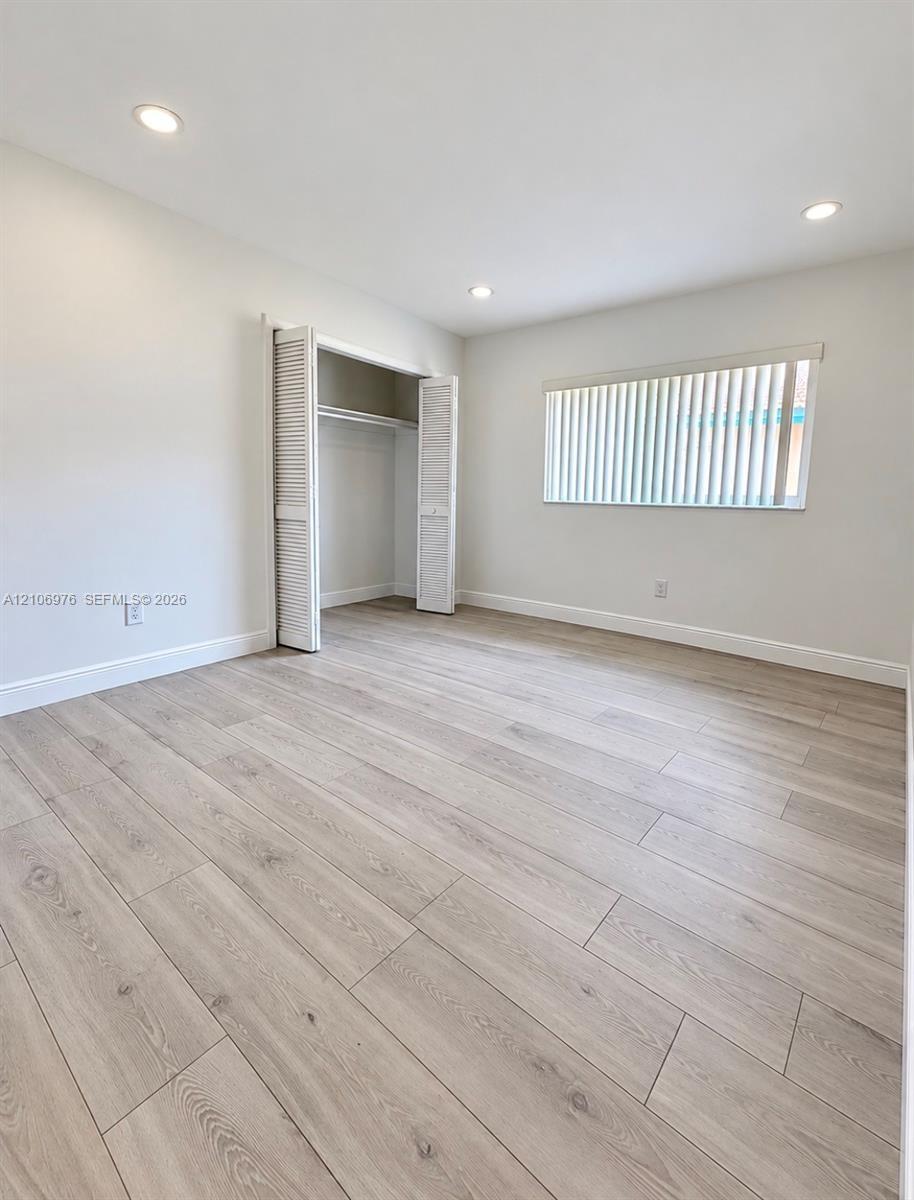 Neutral-toned wood-finish flooring, recessed lighting, and a closet with louvered bi-fold doors