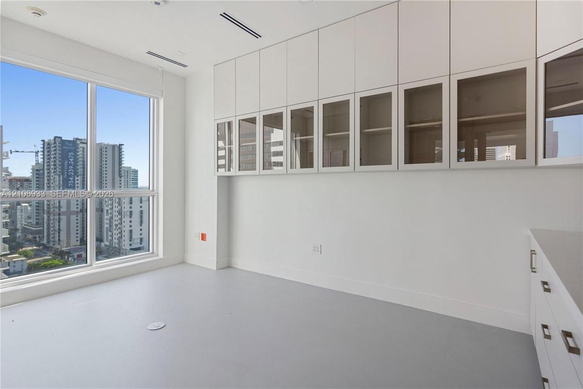 Floor-to-ceiling windows, built-in floor-to-ceiling cabinetry with glass-paneled upper doors, sleek cabinetry hardware, and solid-surface flooring