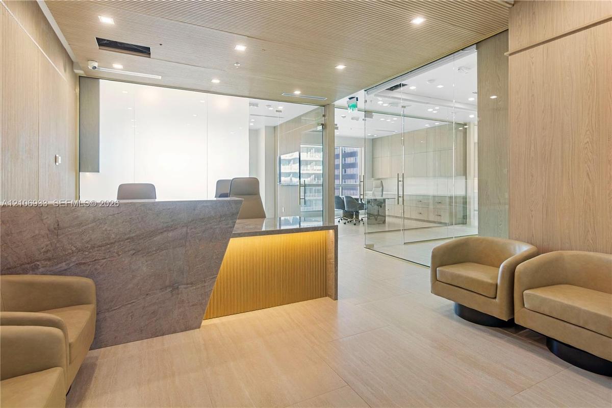 Reception area featuring a stone-faced desk with accent lighting, light wood-finished wall paneling, glass-enclosed office partitions, recessed ceilin
