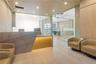 Reception area featuring a stone-faced desk with accent lighting, light wood-finished wall paneling, glass-enclosed office partitions, recessed ceilin