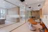 Floor-to-ceiling glass partitions, custom light-wood cabinetry, recessed ceiling lighting, light-toned stone-finish flooring, and built-in quartz coun