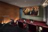 Media room featuring tiered flooring, wood-panel wall accents, recessed ceiling lighting, and integrated wall-mounted projection screen