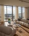 Floor-to-ceiling glass windows, wide-plank wood-finish flooring, and an expansive balcony featuring a glass railing