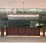 Large-scale linear chandelier with crystalline fringe, wood-veneer floating desk with base accent lighting, and full-height green-toned stone feature 