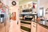 Kitchen featuring stainless steel appliances, dark stone-finish countertops, white cabinetry with glass-front uppers, and light-toned tile flooring
