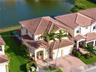 Two-story stucco exterior featuring a multi-gabled tile roof, paver driveway, two-car garage, and waterfront location