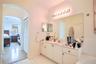 Bathroom featuring a white vanity cabinet with an integrated countertop and sink, wall-spanning mirror, multi-bulb vanity lighting, and arched archite