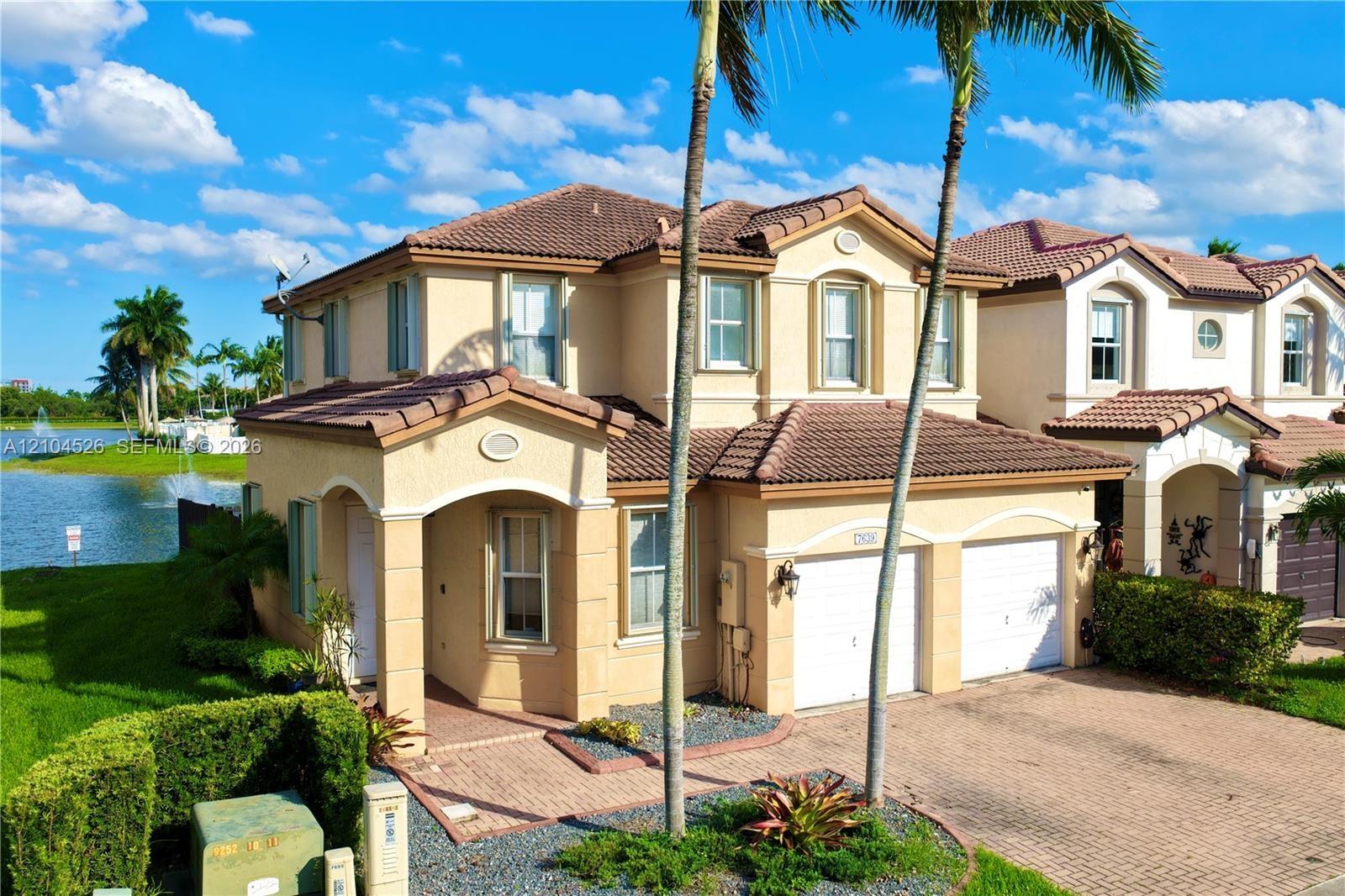 Two-story stucco exterior featuring a tiled roof, arched entryway, brick-paver driveway, and two-car garage