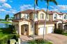 Two-story stucco exterior featuring a tiled roof, arched entryway, brick-paver driveway, and two-car garage