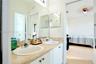 Dual-sink vanity with a natural stone countertop, white cabinetry, chrome-finish faucets, and an expansive wall-mounted mirror