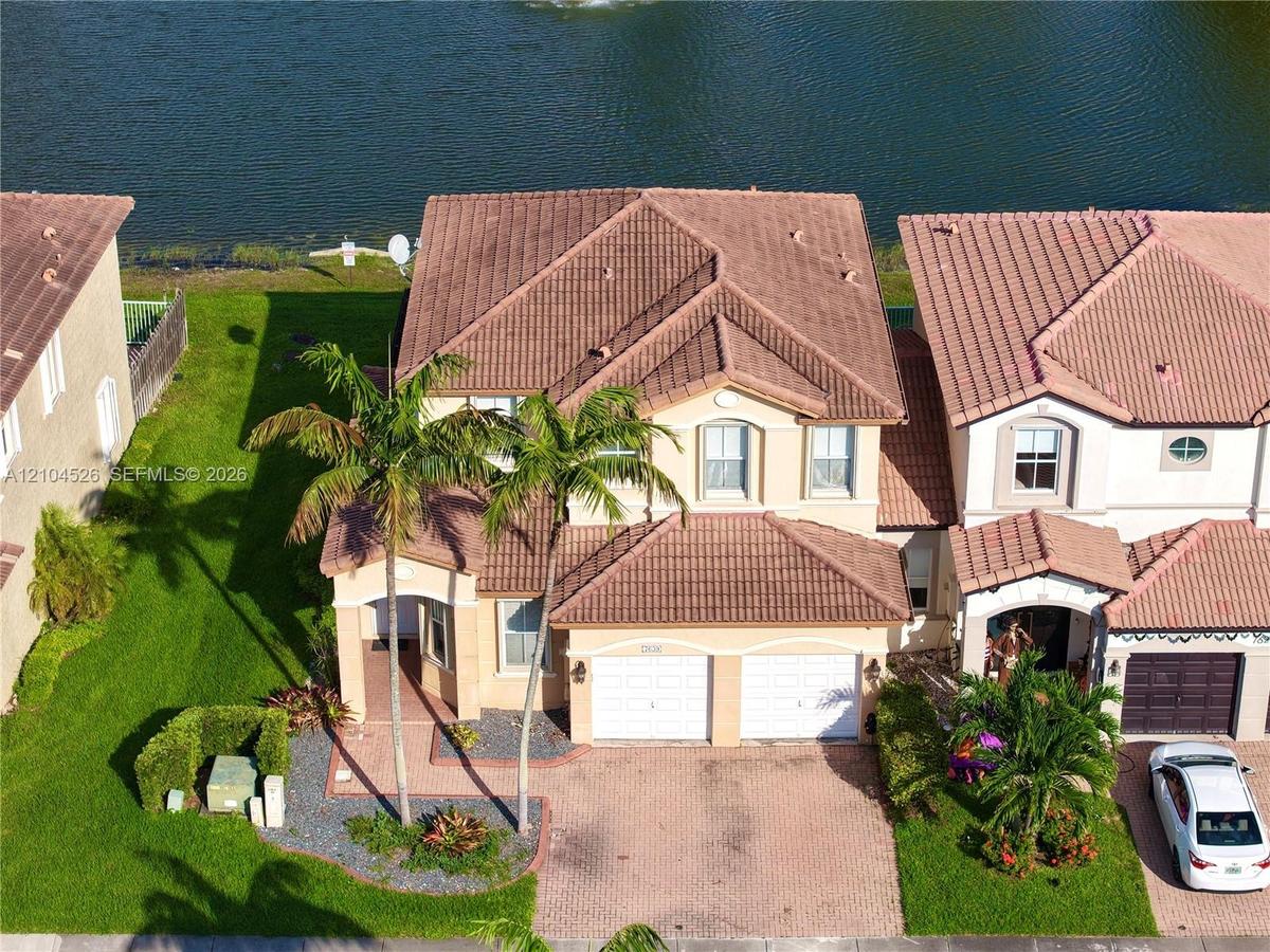 Two-story residence featuring a terracotta-tiled roof, paver driveway, two-car garage, manicured landscaping, and direct water frontage