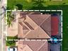 Aerial perspective featuring a multi-hipped tile roof, paved driveway, brick-paver patio, and mature palm landscaping