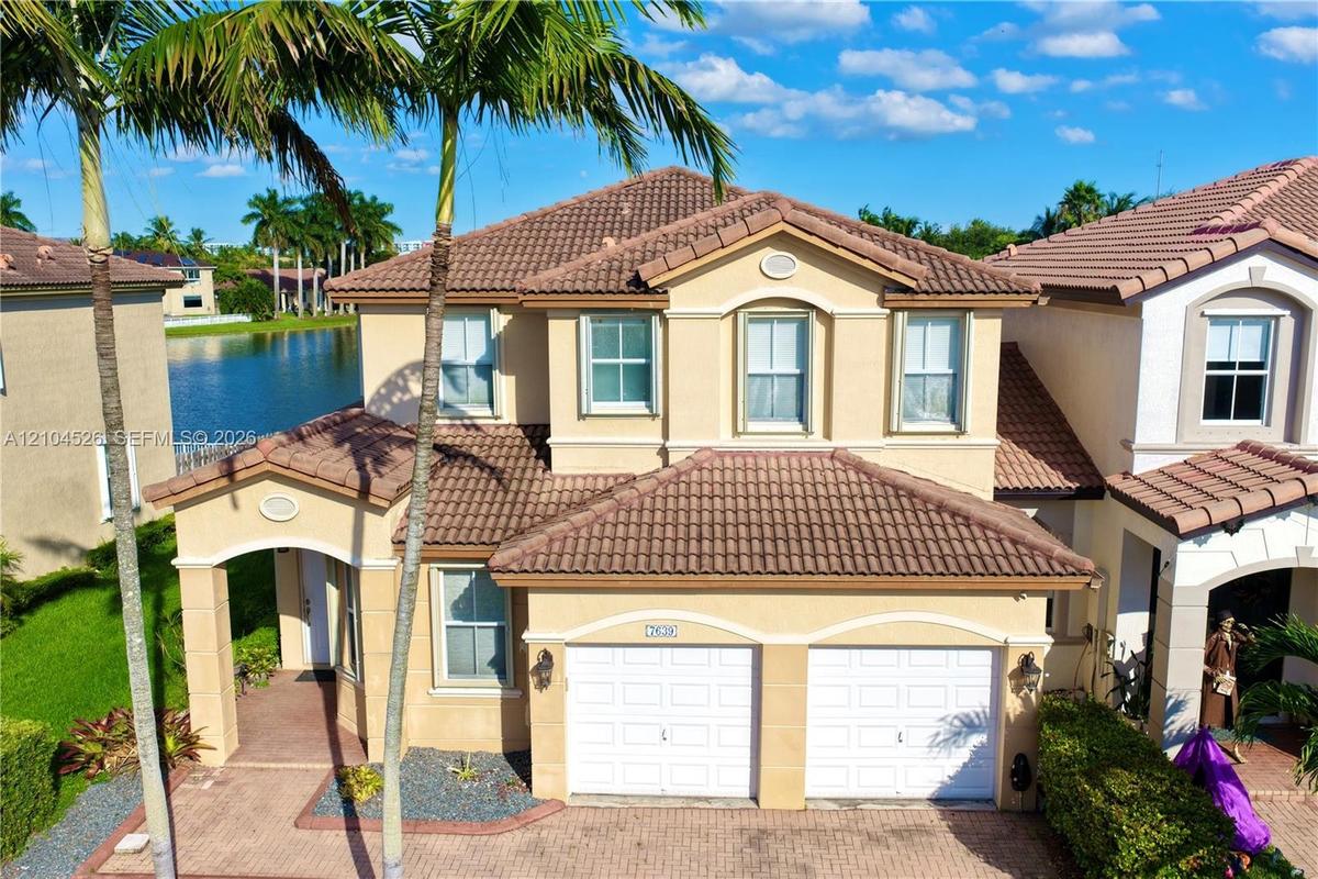 Two-story residence featuring a tile roof, stucco exterior, two-car garage, paved driveway, and water frontage
