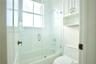 Bathroom featuring a tub-shower combination with a glass door enclosure, white tile surround, integrated window, and built-in upper cabinetry
