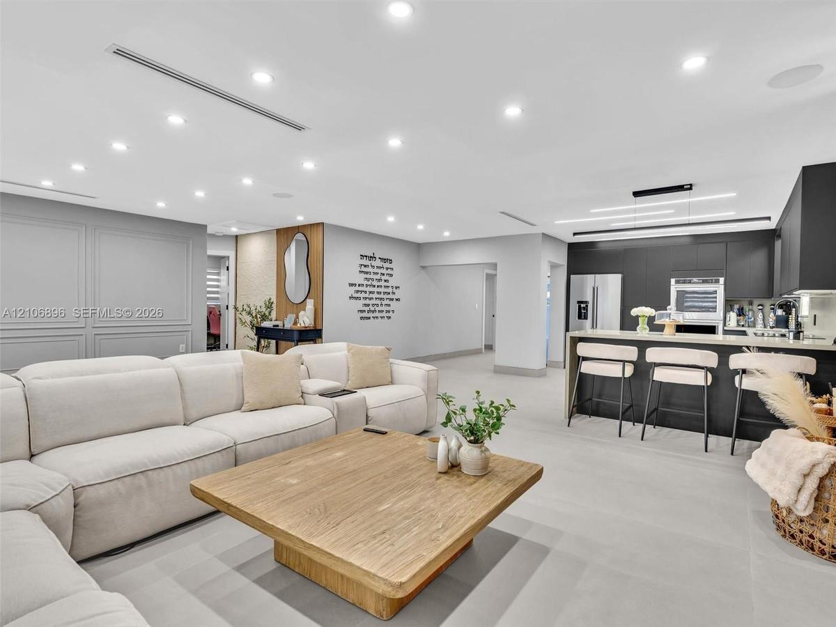 Open-concept interior featuring recessed ceiling lighting, matte black flat-panel cabinetry, a stone-topped kitchen island, neutral large-format floor