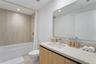 Bathroom featuring a vanity with light-tone wood-finish cabinetry, a solid-surface countertop with an integrated sink, a large frameless mirror, and a