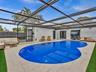 Screen-enclosed pool area with stone tile decking, synthetic turf accents, and perimeter fencing