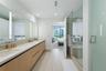 Dual-sink vanity with light wood-finish cabinetry, solid-surface countertop, full-width vanity mirror with integrated vertical lighting, and glass-enc
