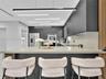 Modern kitchen featuring charcoal cabinetry, expansive stone-surface island, minimalist linear pendant lighting, built-in stainless steel double wall 