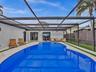 Screen-enclosed pool area featuring concrete decking, synthetic turf accents, and dual sets of French doors