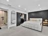 Bedroom featuring large-format tile flooring, a geometric paneled accent wall, sliding dark-finish wardrobe doors, and recessed ceiling lighting