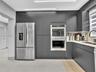 Sleek charcoal cabinetry, stainless steel double wall ovens, French door refrigerator, light-toned countertop, and integrated linear overhead lighting