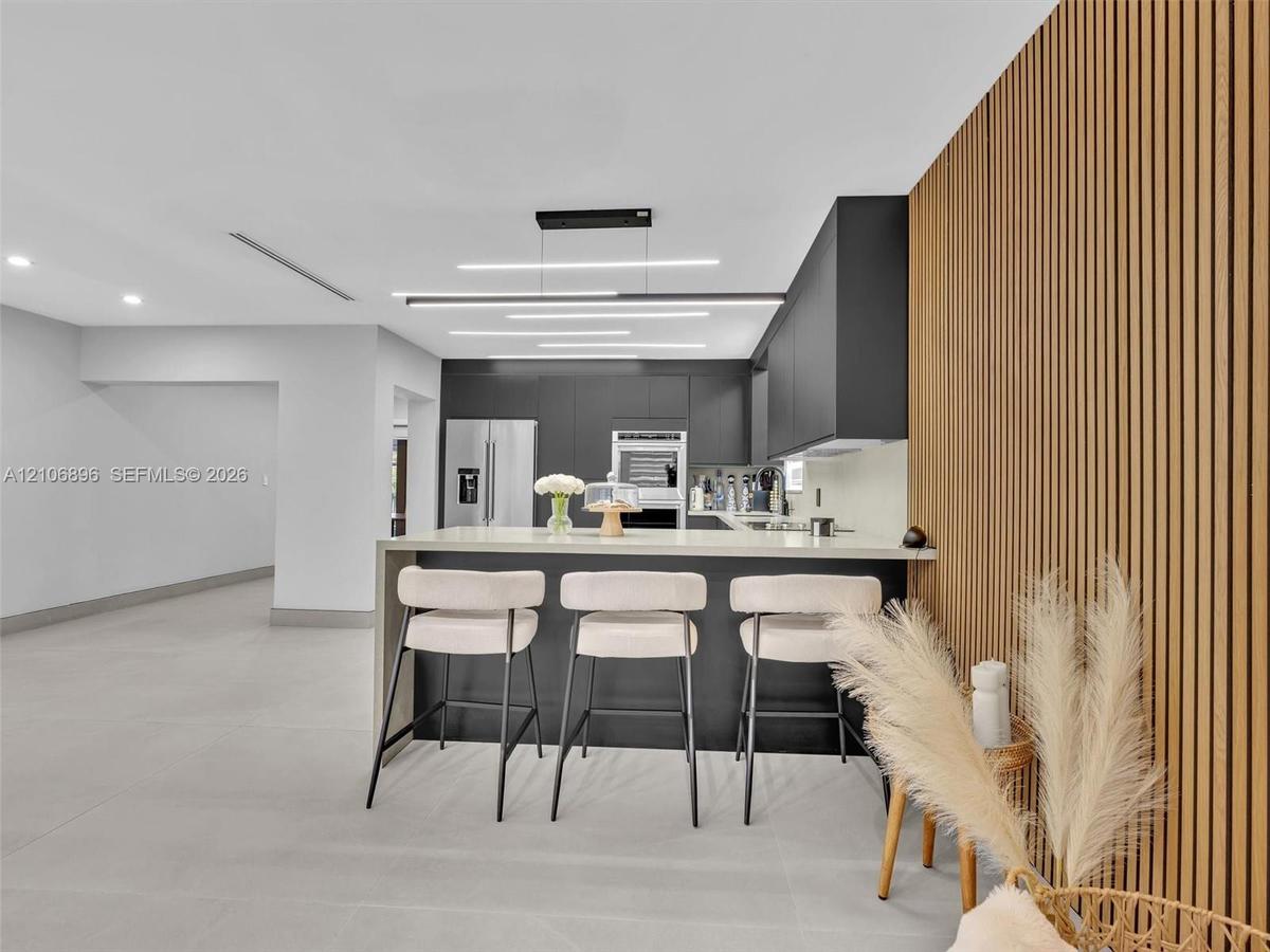Kitchen featuring matte dark cabinetry, a waterfall-edge island with stone-finish countertop, linear LED pendant lighting, and a floor-to-ceiling wood