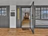 Entryway featuring dark vertical slatted exterior siding, wood-finish tile flooring, matte black grid-pane windows, and dual vertical wall-mounted sco