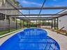 Screened-in outdoor living area featuring a custom-shaped swimming pool, paved pool deck, and synthetic turf lawn bordered by perimeter fencing