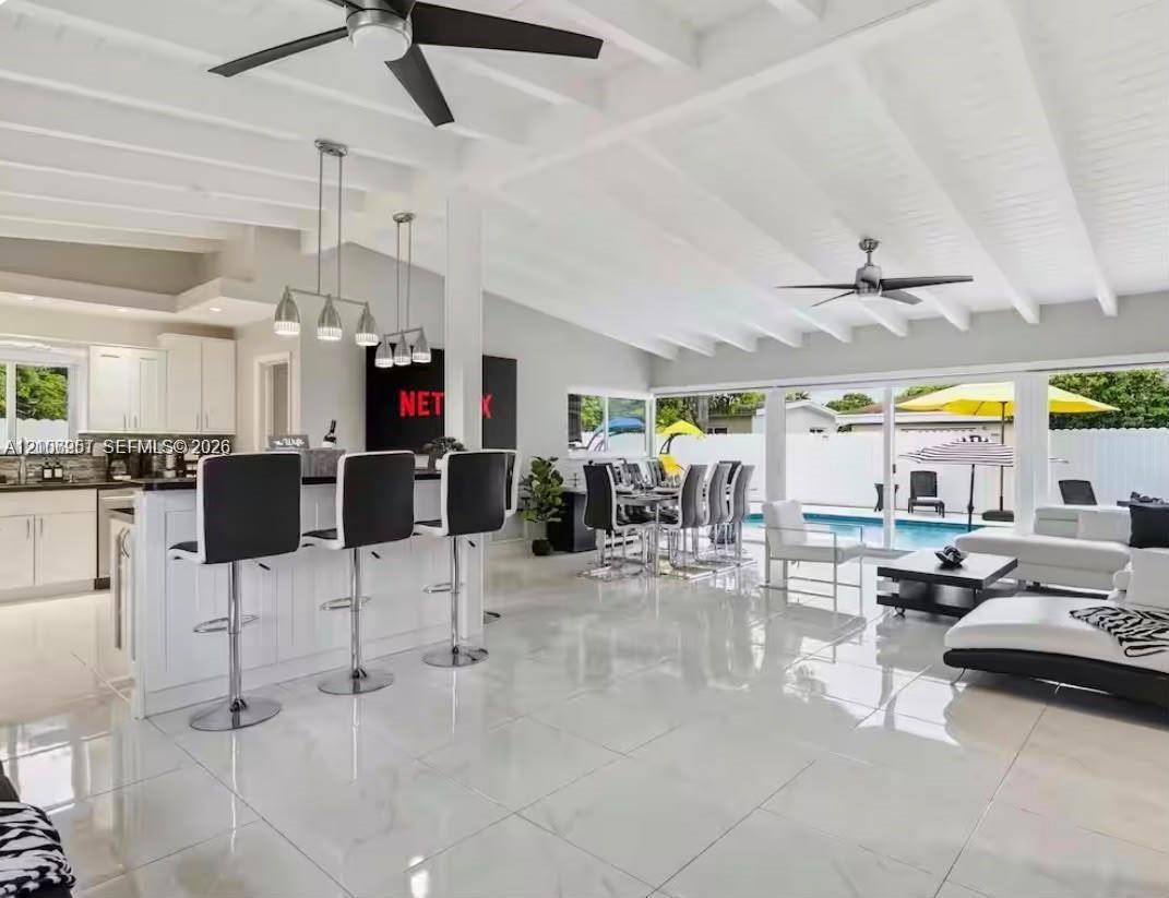 Open-concept interior featuring vaulted, beamed ceilings, oversized tile flooring, a kitchen island with stone countertops, and multiple sliding glass