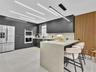 Modern kitchen featuring flat-panel cabinetry, a waterfall-edge stone island, linear LED ceiling lighting, integrated double wall ovens, and a vertica