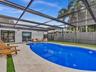 Screened pool enclosure featuring a custom-shaped swimming pool, light-toned stone pool deck with integrated turf detailing, and a high-privacy wood f