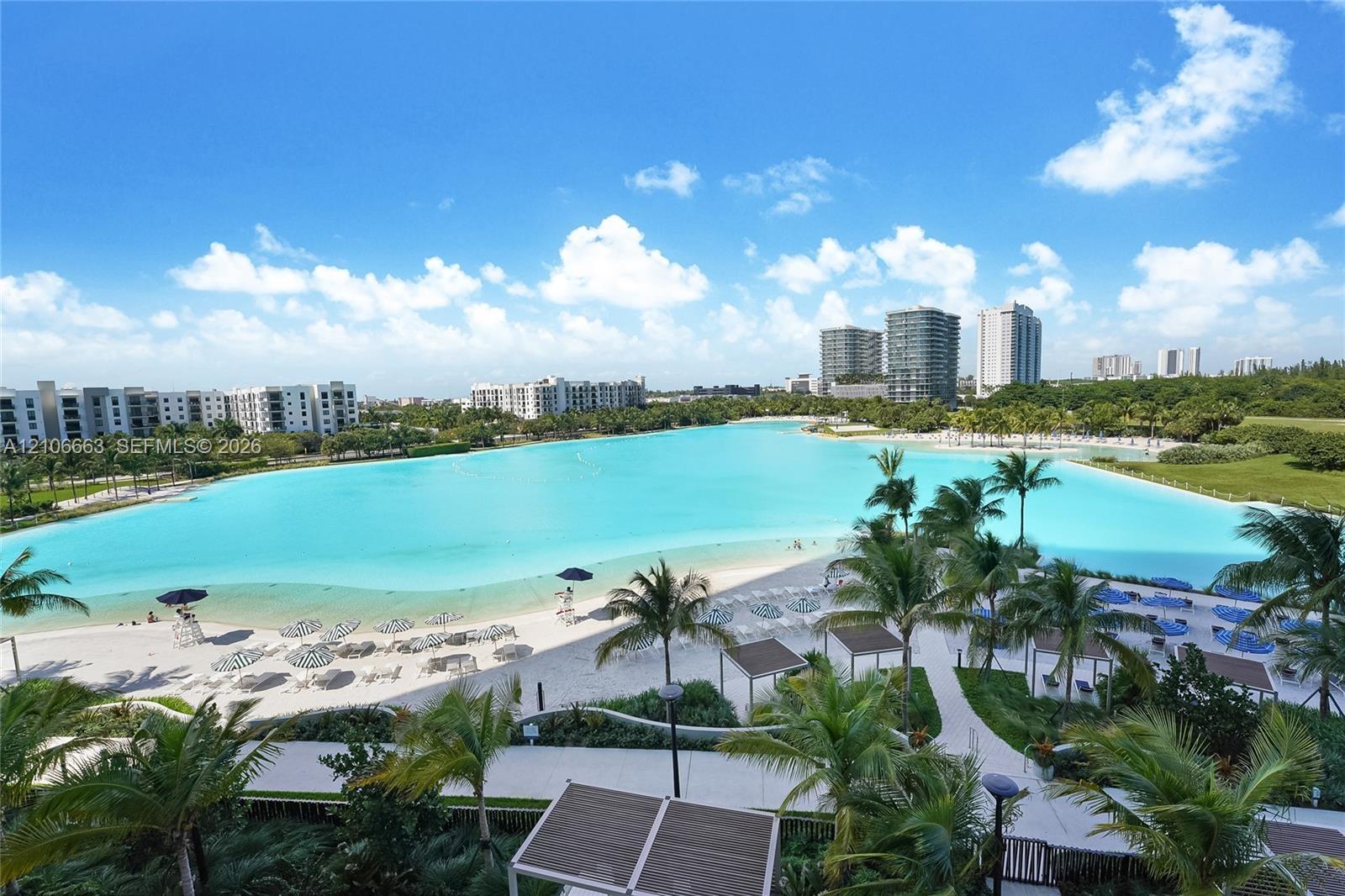 Expansive turquoise lagoon, white sand beach, paved walkways, mature palm trees, and structural shade cabanas
