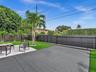 Expansive backyard featuring a concrete patio with a hexagonal pattern, synthetic turf lawn, perimeter wood privacy fencing, and mature palm trees