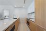 Contemporary kitchen featuring white flat-panel upper cabinetry, light wood-finish lower cabinetry, stone-style countertops with integrated backsplash