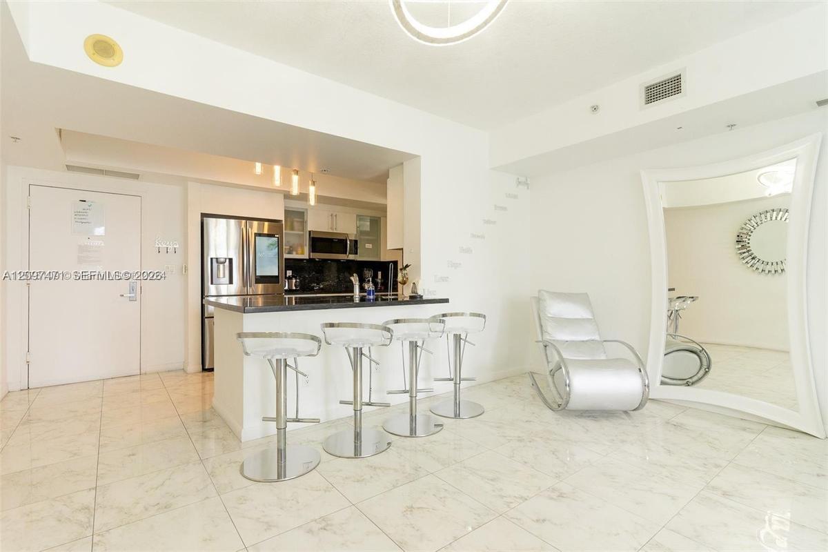 Kitchen area featuring a stone-topped breakfast bar, stainless steel refrigerator, dark cabinetry, recessed lighting, and polished stone-finish floori