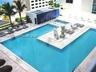 Outdoor swimming pool featuring a central paved island, built-in steps, surrounding stone-finish deck, and palm trees