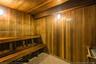 Sauna featuring wood-plank walls and ceiling, tiered built-in wooden bench seating, wall-mounted light fixtures, and tiled flooring