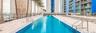 Rectangular swimming pool featuring metal access railings, a concrete deck, and perimeter palm trees
