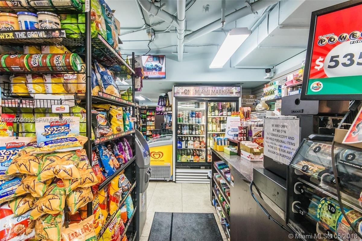 Retail space featuring built-in industrial shelving, commercial glass-front refrigeration units, a stone-surfaced transaction counter, and overhead fl