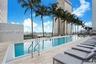 Rectangular lap pool featuring stone-tile decking, stainless steel ladder railings, and perimeter palm trees
