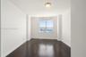 Room featuring wood-finish flooring, white walls, and a large window showcasing water and harbor scenery, complemented by a flush-mount ceiling light 
