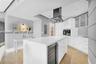 Modern kitchen featuring a central island with an integrated wine cooler, sleek white cabinetry, stainless steel range hood, built-in wall oven, and l