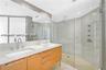 Dual-sink vanity with light-tone cabinetry and stone countertop, complemented by a walk-in glass-enclosed shower featuring multi-head wall-mounted fix