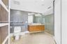 Bathroom featuring a wood-finish floating vanity with a dual-faucet countertop, glass-enclosed shower, mosaic tile wall, and recessed lighting