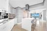 Modern kitchen featuring white flat-panel cabinetry, a central island with a solid-surface countertop, stainless steel vent hood, built-in coffee syst