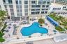 Multi-level building exterior featuring an organic-shaped swimming pool, paved pool deck, built-in cabanas, and mature palm trees