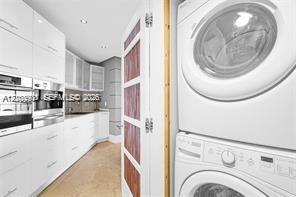 High-gloss white cabinetry, integrated stainless steel appliances, stacked laundry unit, and a paneled wood-finish door
